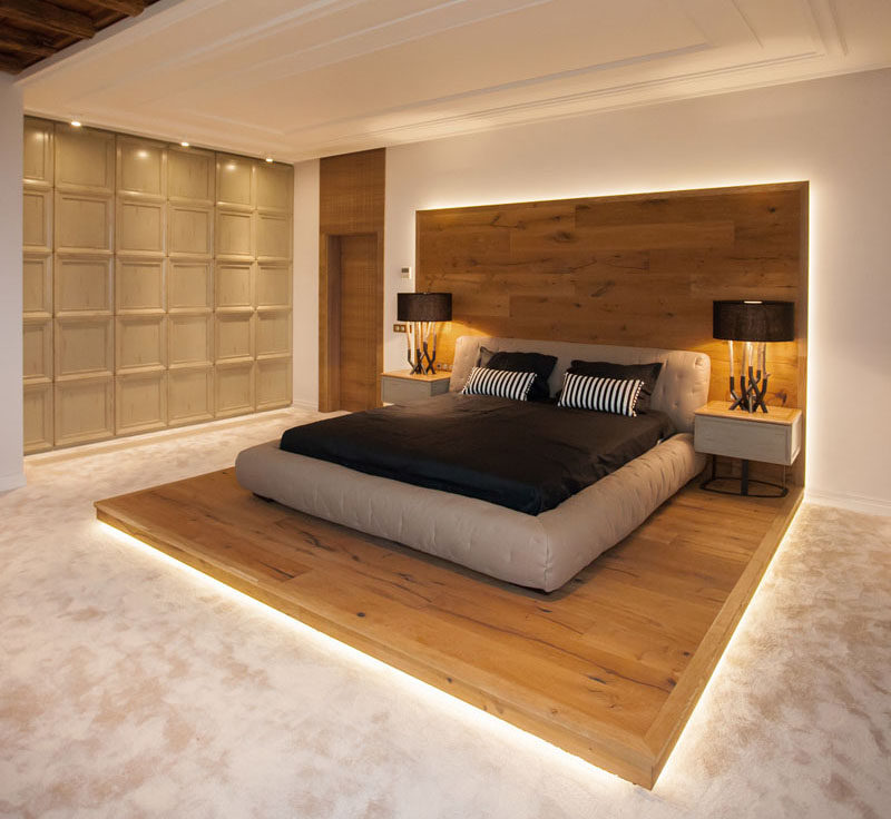 This modern chalet-inspired bedroom features a raised bed on a wood platform. The wood platform is highlighted by hidden lighting to accent the feature and create a warm ambiance. #RaisedBed #WoodPlatform #ModernBedroom #InteriorDesign