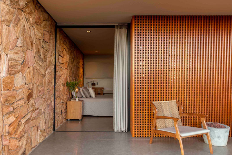 This modern bedroom has a stone wall behind the bed that flows from the inside to the outside, and a sliding door opens the bedroom to the deck. #ModernHouse #StoneWall #ModernBedroom