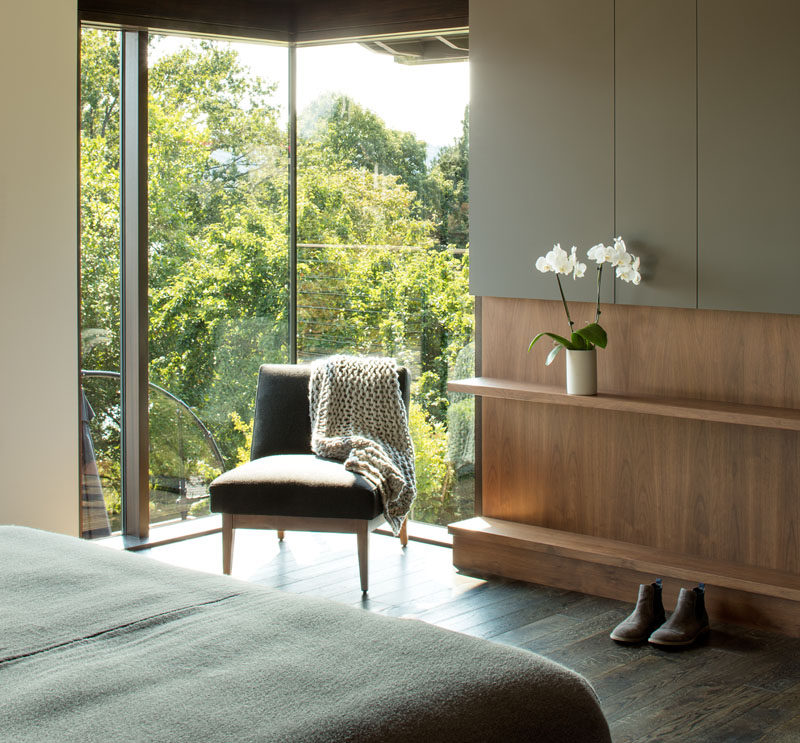 This modern bedroom has corner windows that provide natural light and views of the trees, while a built-in wood shelf allows for a touch of nature to be displayed inside. #ModernBedroom #Shelving #Windows