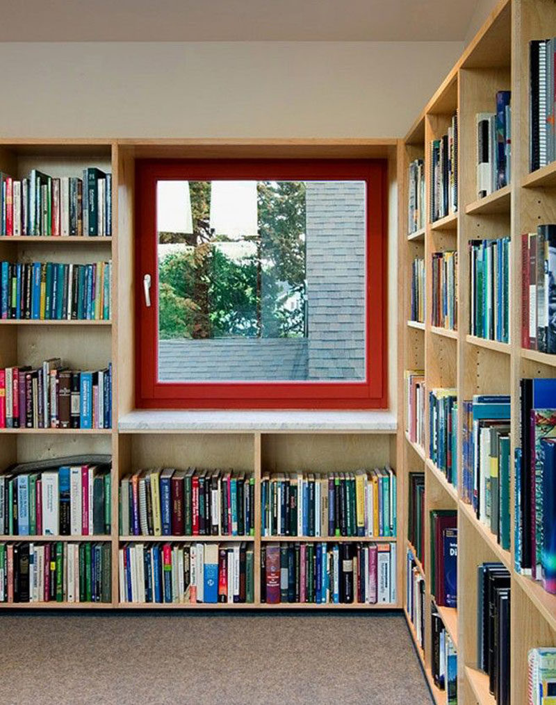 This home library has built-in wood shelves and a window with a bright red window frame. #Library #HomeLibrary #Shelving