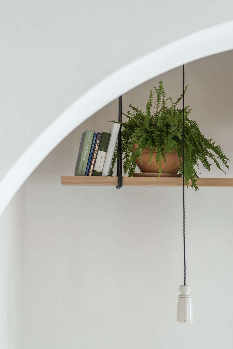 Hanging above a dining area in a modern cafe is a simple wood shelf that's home to plants and books. #Shelving #InteriorDesign #Shelf #HangingShelf