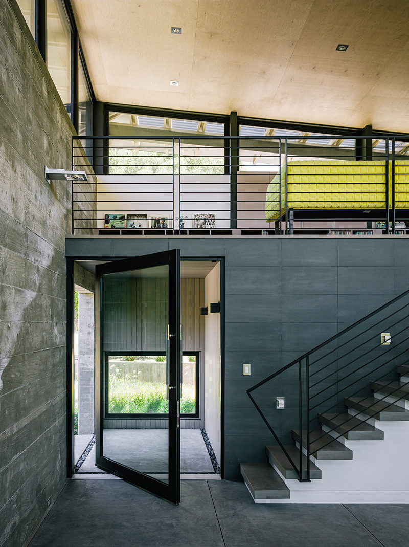 A pivoting glass door welcomes you to this modern house, and the black frame matches the handrails and window frames. #PivotingGlassDoor #PivotingDoor #FrontDoor