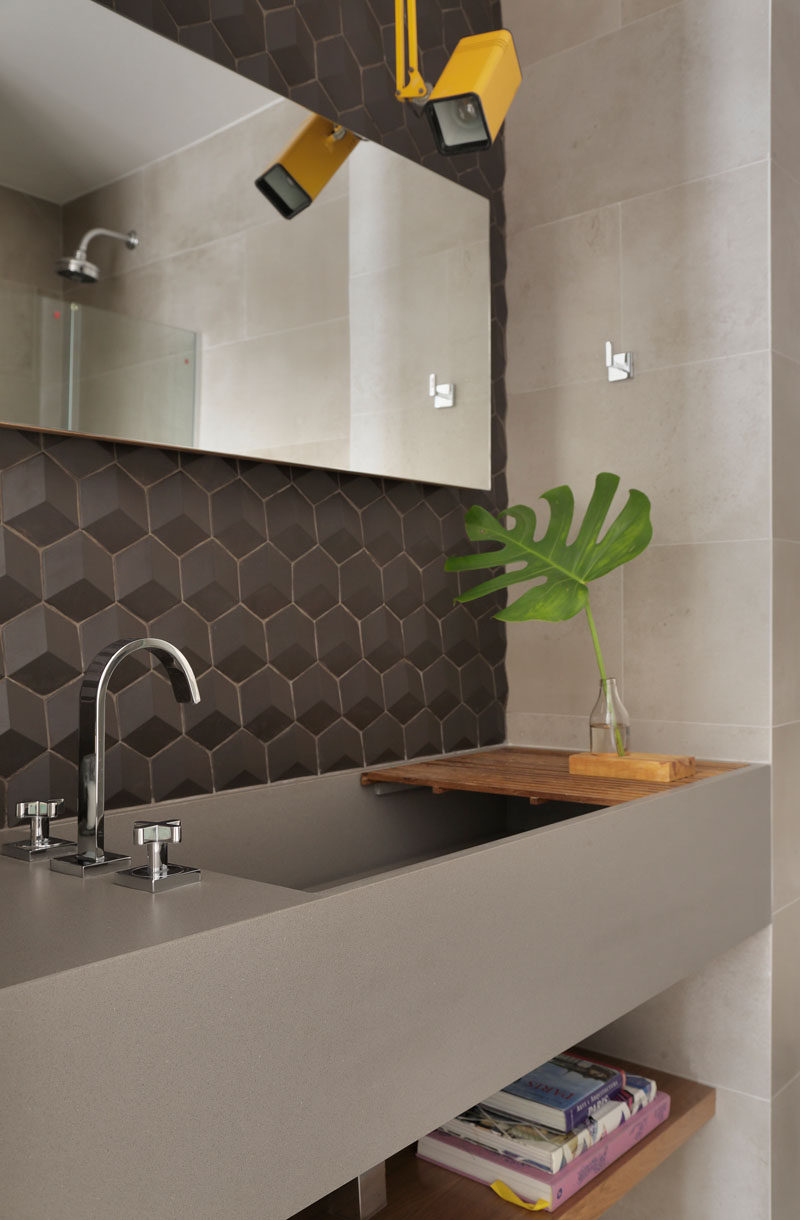 Grey tiles and a grey vanity with a large deep sink set the tone for this modern bathroom. A pop of color has been added with the use of a single yellow light. #ModernGreyBathroom #ModernBathroom #BathroomDesign