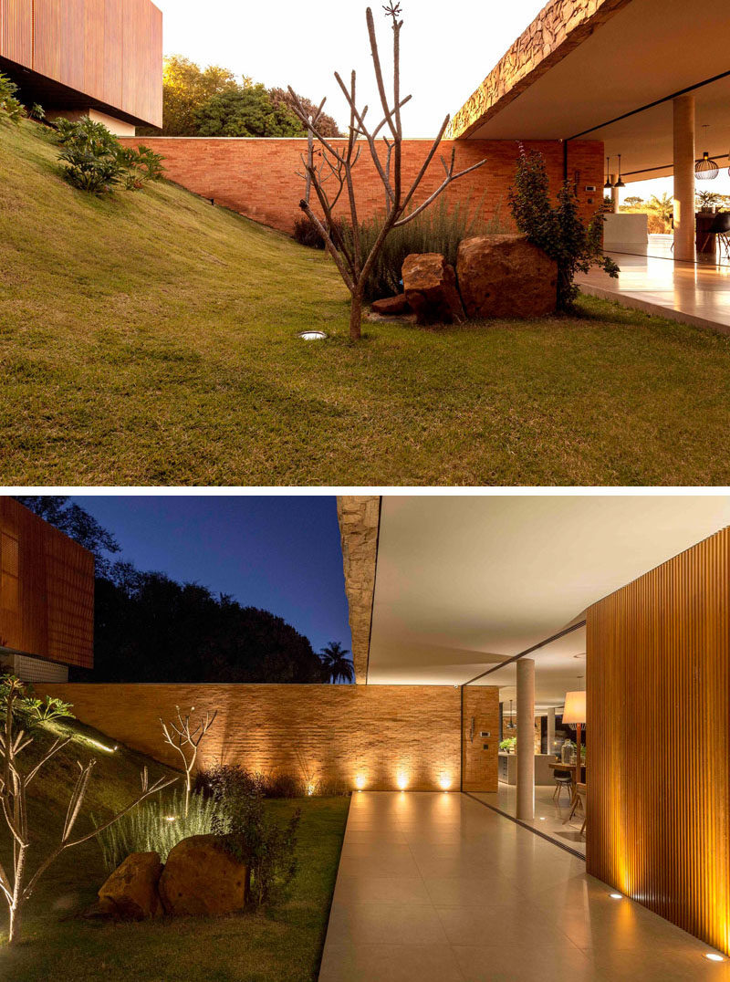 Upon entering this modern house, there's a grassy hill with a few plants and boulders. A covered path leads to the social areas of the home. #Landscaping #Architecture