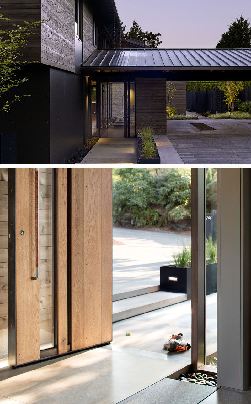 Upon arriving at this modern house, there's a carport that has views of a courtyard and a path provides access to the deck around the side of the home. A large wood and glass front door greets visitors. #Carport #ModernHouse #WoodFrontDoor #ModernFrontDoor