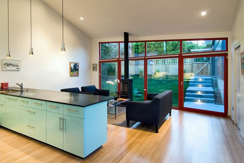 A small backyard is located of the living room in this modern house, with large doors providing access to the outdoor space. #Windows #Backyard #InteriorDesign #LightBlueKitchen