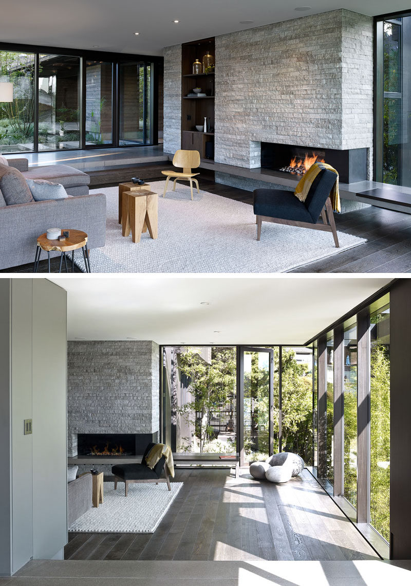 This modern living room is slightly stepped down from the hallway. A stone accent wall has a built-in wood bookcase and fireplace. Large floor-to-ceiling windows flood the room with natural light. #Fireplace #StoneWall #AccentWall #ModernLivingRoom #Windows