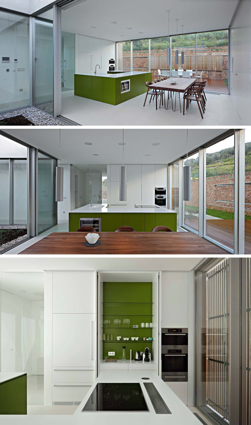 In this modern kitchen, an island with an olive green base and a white counter compliments the white cabinets, that when opened, have an olive green interior. #ModernKitchen #OliveGreen #InteriorDesign #KitchenCabinets