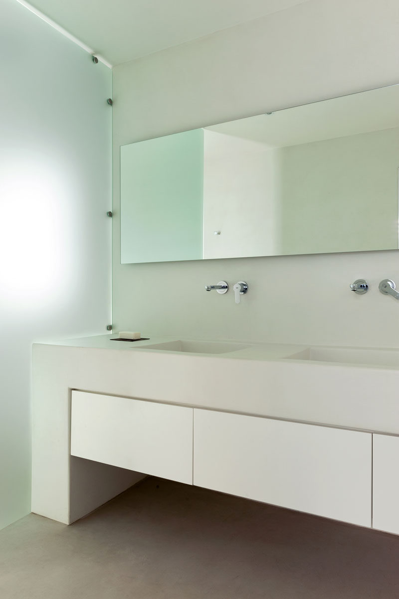 In this modern master bathroom, a large built-in vanity with storage provides plenty of space for dual sinks, while frosted glass acts as a shower screen. #ModernBathroom #Bathroom #Vanity