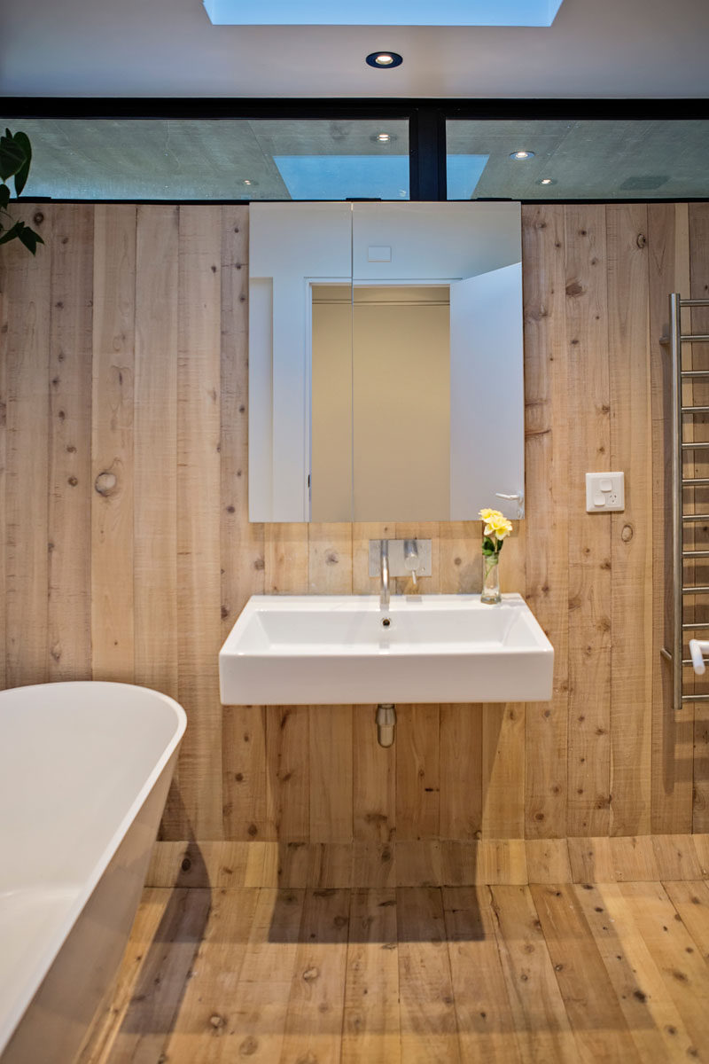 A simple color palette of wood and white has been used for the design of this modern bathroom, with a skylight adding natural light during the daytime. #ModernBathroom #Wood #WoodBathroom #Skylight