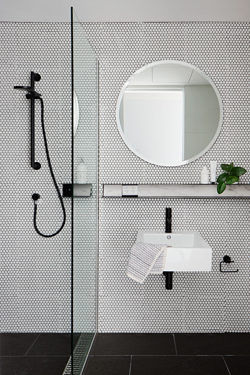 In this bathroom, white floor-to-ceiling penny tiles have been used to line the wall, while a round mirror and black accents complete create a modern look. #ModernBathroom #RoundMirror #PennyTiles #BathroomDesign #InteriorDesign