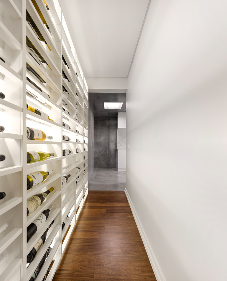 This modern apartment has a backlit wine wall in a hallway that connects the entrance hall to the kitchen. #WineStorage #WineWall
