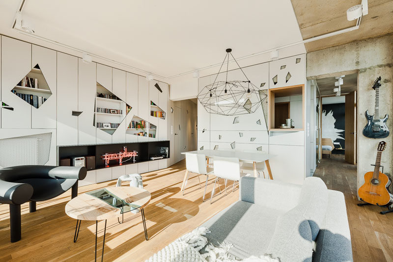 This modern apartment has a wall of white cabinets that have geometric cut-outs in the doors to add an artistic feature to the interior. #Cabinets #Geometric #LivingRoom #InteriorDesign #ModernLivingRoom