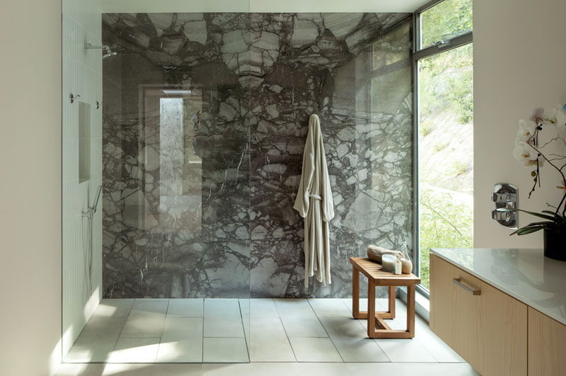 In this modern bathroom, a dark stone accent wall highlights the glass enclosed shower, while a large window provides ample natural light. #StoneWall #GlassEnclosedShower #ModernBathroom