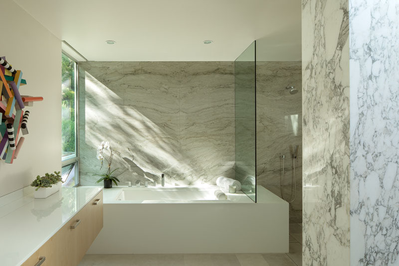 In this modern bathroom, a built-in bathtub has been positioned to take advantage of the tree views, and a glass partition separates the shower from the rest of the bathroom. #ModernBathroom #StoneWalls #BathroomDesign