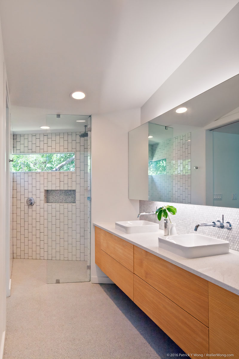 In this modern bathroom, there's a large double-sink vanity and a walk-in shower with a glass shower door and white tiles. #ModernBathroom #BathroomDesign