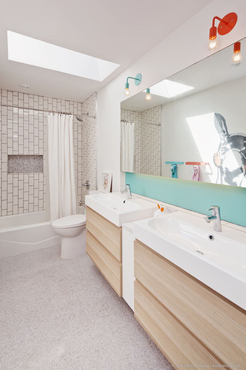 This modern kids bathroom has a skylight, colorful lamps, backsplash and towel racks, and a fun animal mural on the wall. #KidsBathroom #BathroomDesign #ModernBathroom