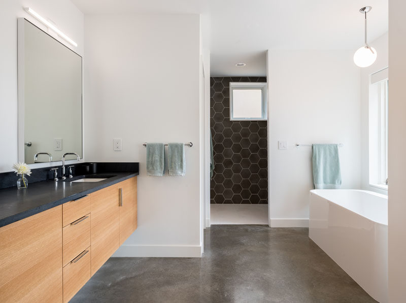 In this modern bathroom, white walls have been paired with dark grey hexagonal tiles, a concrete floor and a wood vanity with a dark countertop. #ModernBathroom #GreyTiles