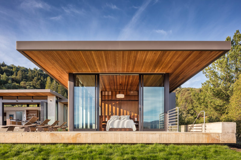 Sliding glass doors open this bedroom to the outdoors, while the wood ceiling continues through to the outside and becomes an overhang that provides shade on a hot day. #ModernBedroom #BedroomDesign #WoodCeiling #Overhang #Architecture