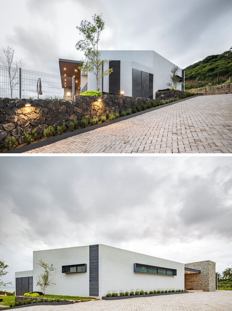 A stone wall with small plants runs alongside the driveway and leads up to the front door of this modern house. #Driveway #Landscaping #StoneWall #ModernHouse