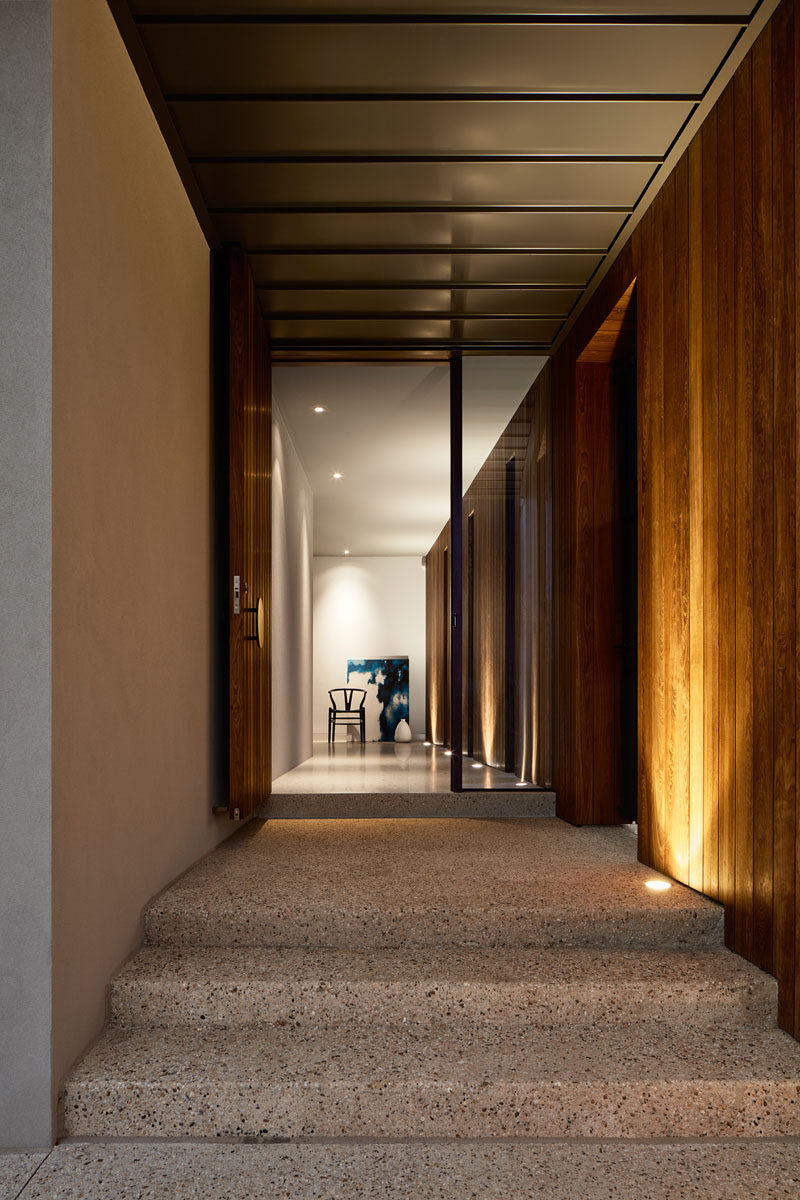 The entryway of this modern house is tucked behind a timber-clad wall with vertical slot windows that frame views of the garden. #Entryway #ModernHouse #Stairs