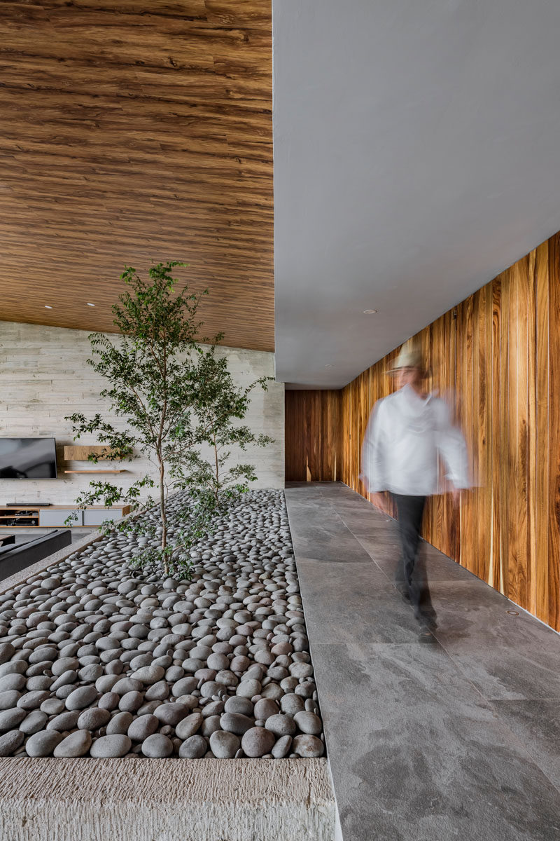 This modern house has a raised walkway that leads to the bedrooms and bathrooms. A small stone covered indoor garden adds a touch of nature to the interior. #IndoorGarden #Stone #InteriorDesign #ModernHouse