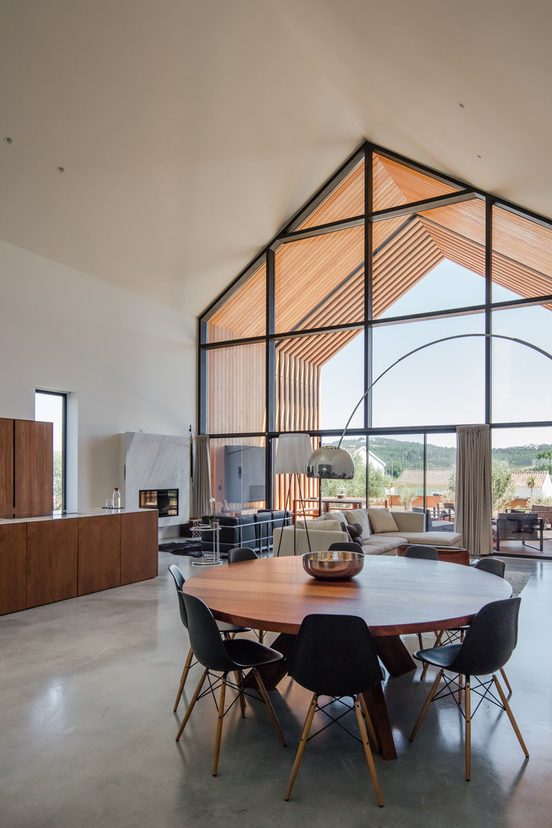 In this modern house, a large round wood dining table is surrounded by black chairs that tie in with the black window frames. #ModernDiningRoom #WoodDiningTable #RoundDiningTable #Windows