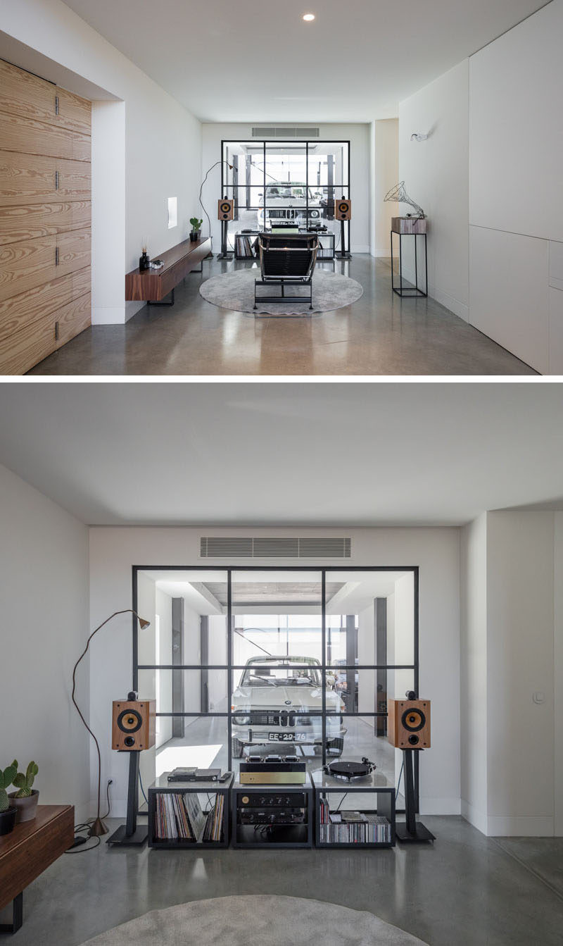 This modern house has a music room, which is set up with a record player and a relaxing lounge chair look out through a black-framed glass wall that provides a view into the garage. #MusicRoom #InteriorDesign #GlassWall