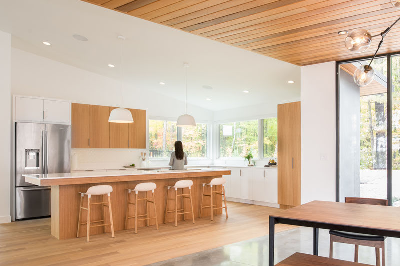 In this modern kitchen, bright white walls are warmed up with the use of white oak cabinets, and large windows let the surrounding tree views become the highlight of the kitchen. #ModernKitchen #KitchenDesign