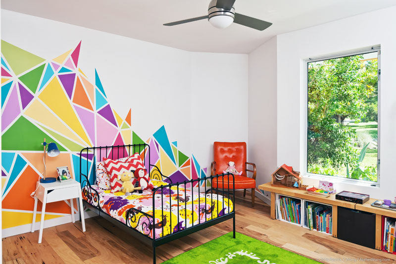 In this modern bedroom, a large, colorful and graphic mural brightens up the white walls, while a window gives views of the gardens. #BedroomDesign #KidsBedroom #ModernBedroom #GraphicMural