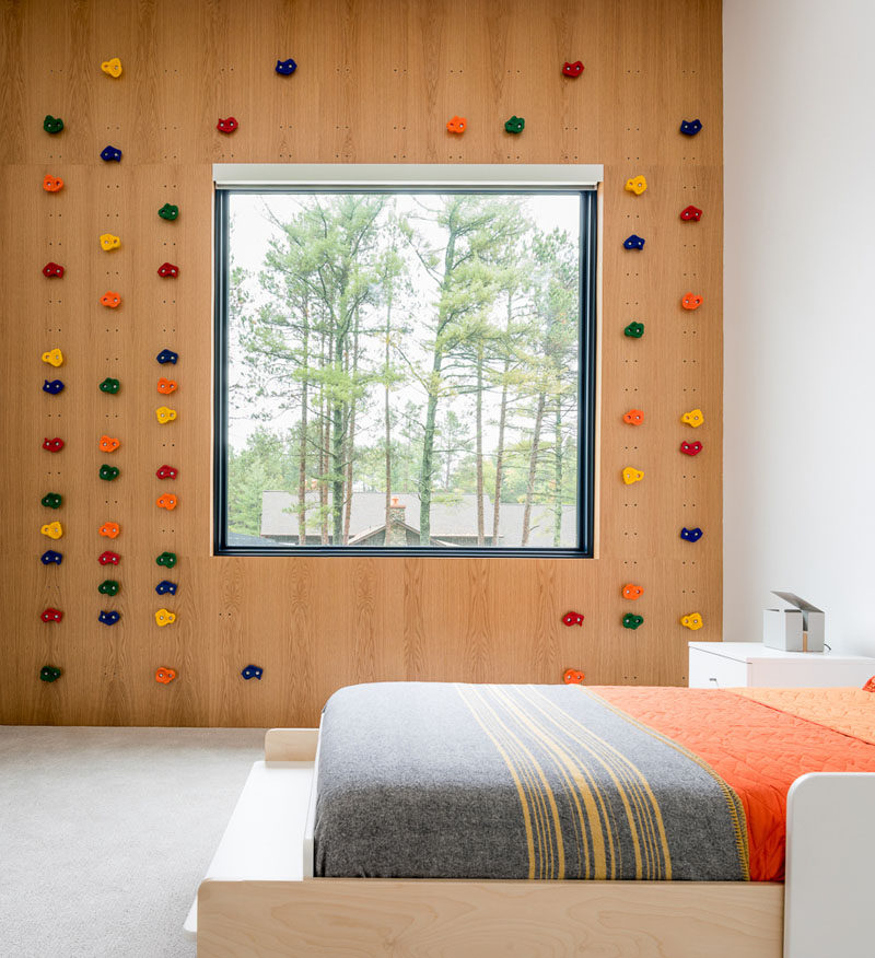 In this modern kids bedroom, a rock climbing wall surrounds the window and small sets of holes in the wood wall allow the 'rocks' to be moved to create a new climbing challenge when needed. #RockClimbingWall #KidsBedroom #BedroomDesign