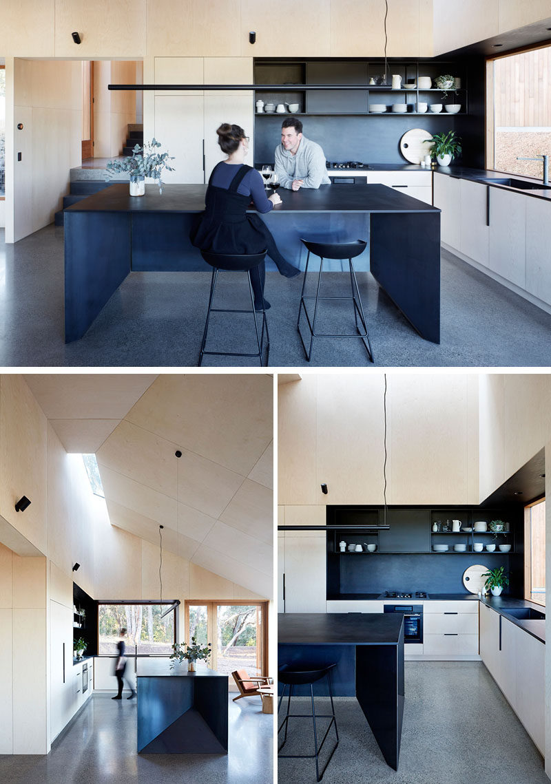 The modern plywood kitchen has been designed as a communal zone with plenty of space. A large black island with seating matches the black shelving, backsplash and countertop, creating a bold and contemporary look. #ModernKitchen #Wood #BlackIsland #KitchenDesign