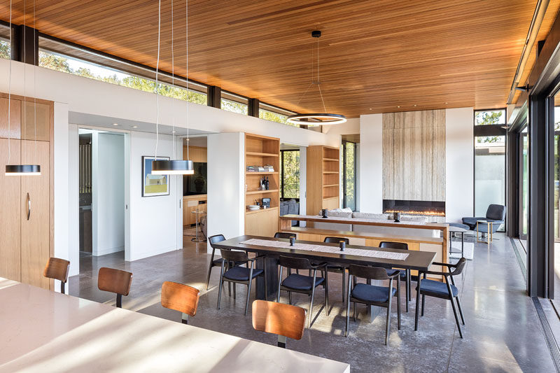 Inside this modern house with an open plan interior, clerestory windows provide a separation between the walls and the wood ceiling, while a large fireplace has a stone accent above it. #Windows #Fireplace #ModernInterior