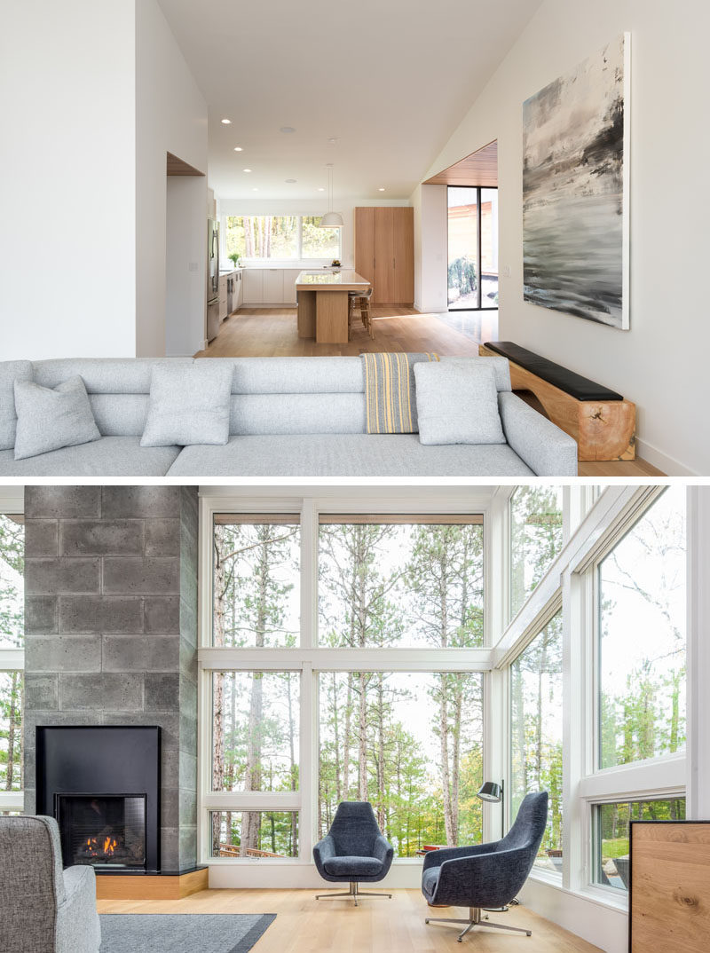 Large windows wrap around this modern living room and show off the tree views, while a fireplace creates a focal point in the room. #ModernLivingRoom #Windows #Fireplace
