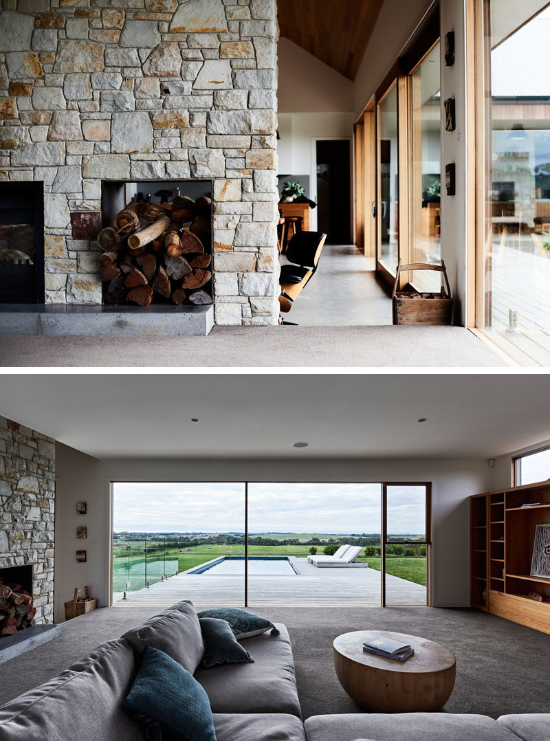 Stepping up from the main social room in this modern ranch-inspired house, is a living room with a built-in shelving unit to house the television. Large windows provide a view of the landscape and pool outside. #StoneFireplace #Windows #LivingRoom