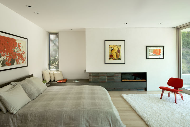 This modern master bedroom looks out over the pool and backyard, while inside, there's a fireplace and a built-in bench for relaxing. #MasterBedroom #Fireplace #SeatingNook