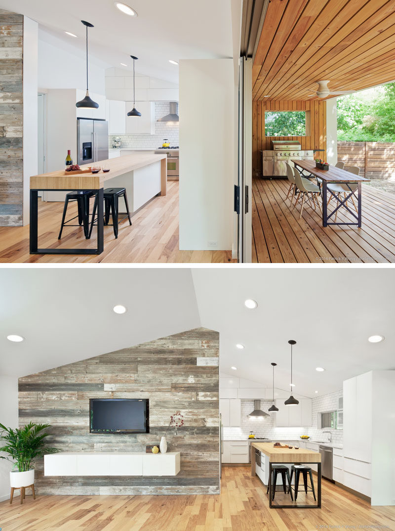 In this modern kitchen, white cabinets are paired with a large island that features a wood counter. Beside the kitchen is a wood accent wall that's home to the television and floating cabinet. #ModernKitchen #KitchenIsland #WoodAccentWall