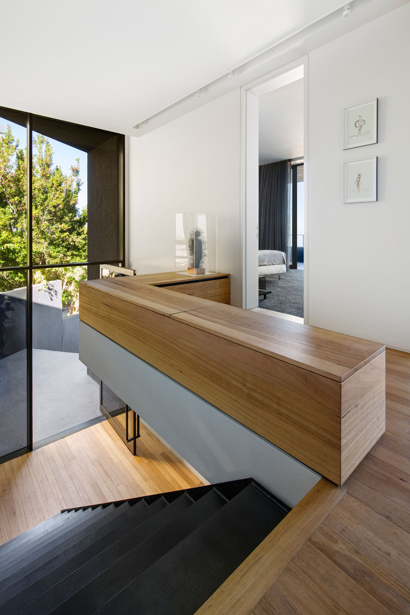 By the front door of this modern house, stairs lead up to the second floor that's home to the bedrooms. Large windows flood the staircase with natural light, while black steel stairs continue the dark theme found throughout the house. #ModernStairs #Windows #InteriorDesign