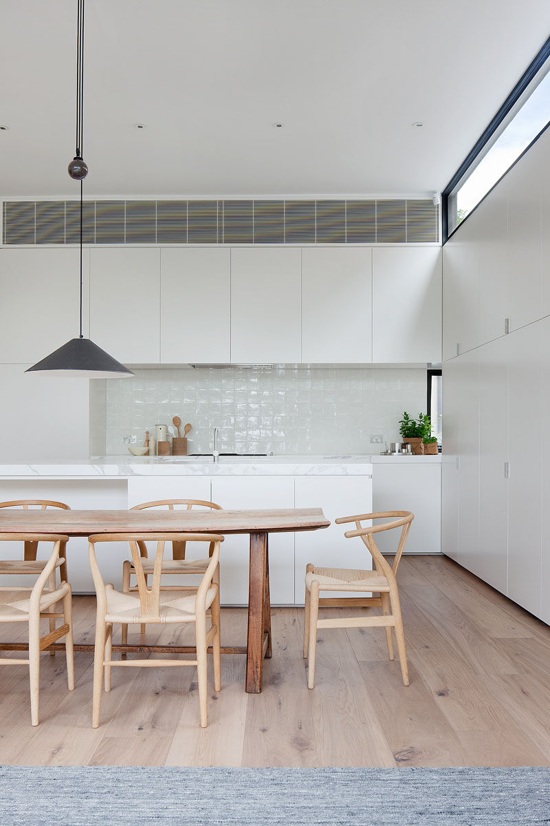 The light wood dining table and chairs, combined with the flooring, add a sense of warmth to the mostly white modern interior. #DiningRoom #WhiteKitchen #WoodFloors #InteriorDesign