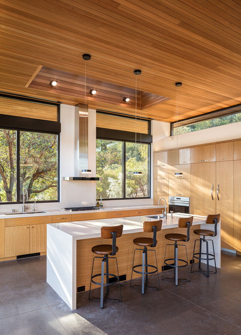 In this modern kitchen, light wood cabinets, white countertops, large windows and a skylight all help to keep the kitchen bright and airy. #ModernKitchen #LightWoodCabinets #WoodCeiling