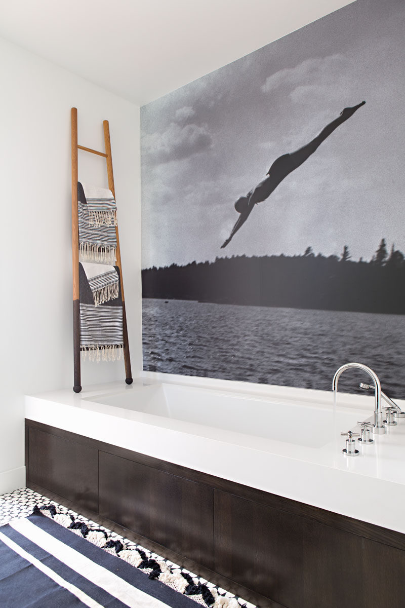 In this modern bathroom, the wall above the bath is covered with art, while a ladder provides a place to hang towels. #BathroomDesign #ModernBathroom