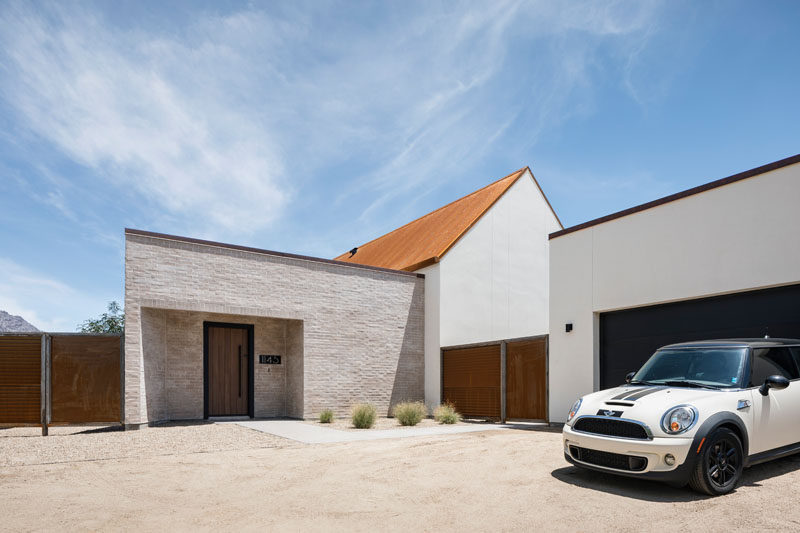 This modern house, with a white and sandy colored brick exterior, features a rusted, corrugated metal roof and black frames around the windows and wood doors. #RustedMetalRoof #ModernHouse #Architecture