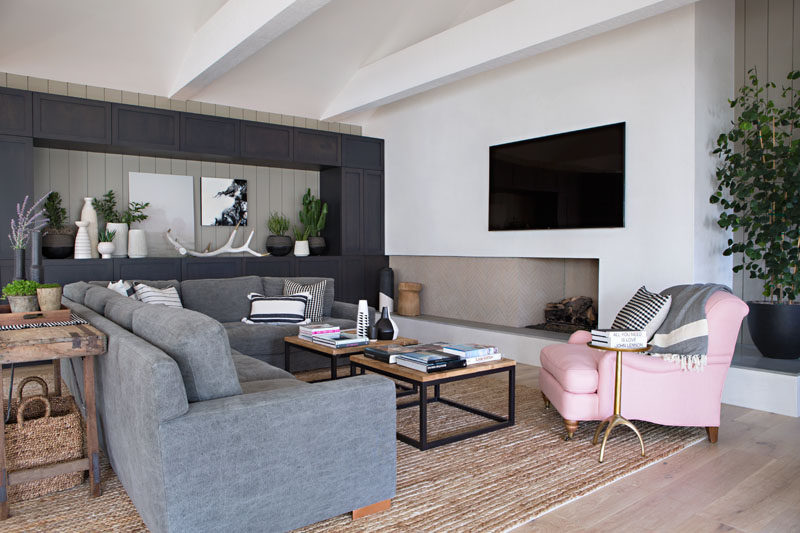 In this contemporary living room, dark cabinetry along one wall creates plenty of storage as well as a place to display favorite items, while a fireplace, comfortable couch and rug, all add a sense of warmth to the room. #LivingRoom #Fireplace #GreyCabinets