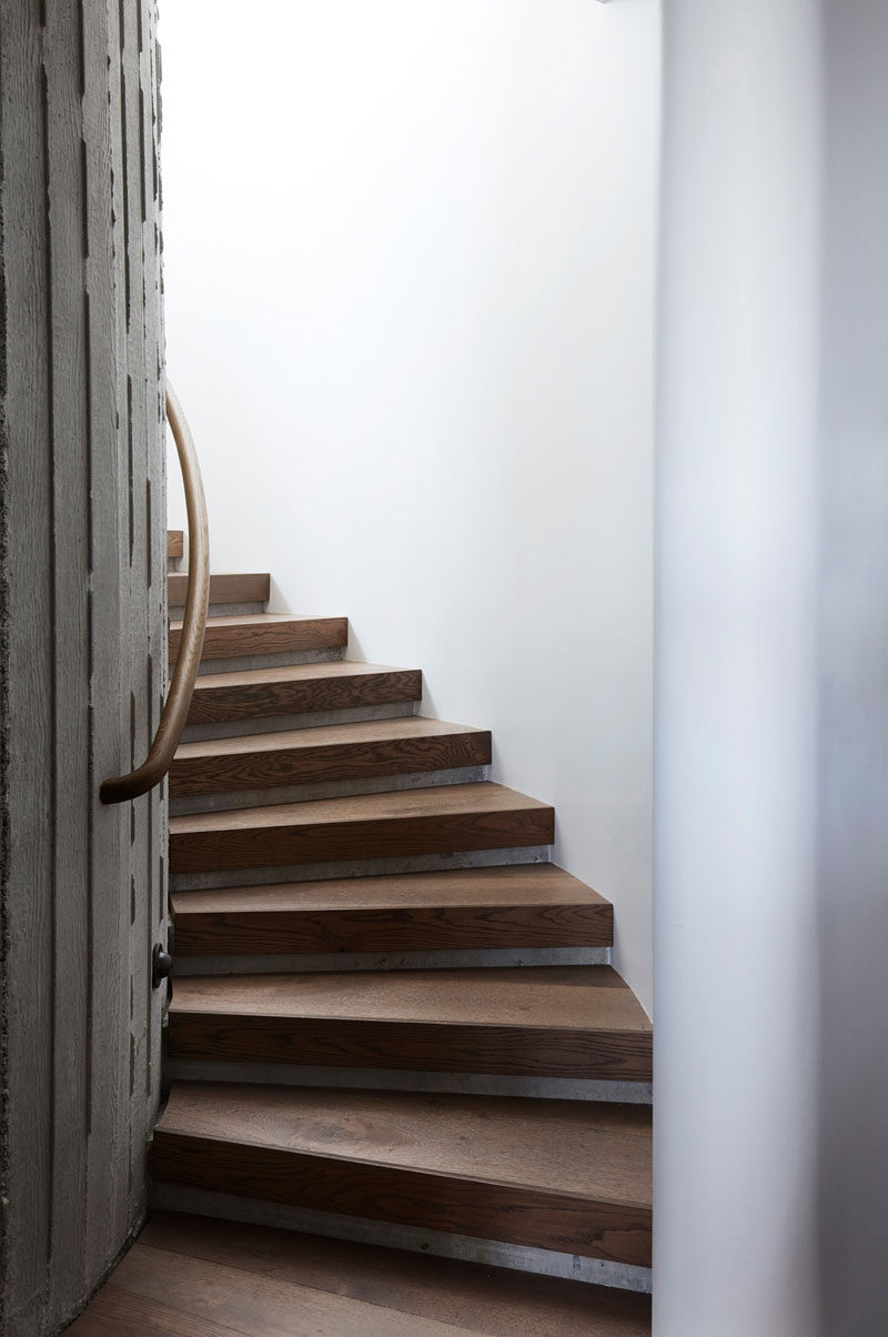 This modern elliptical shaped stairwell has white and concrete walls, and stair treads made from oak. #WoodStairs #CurvedStairs