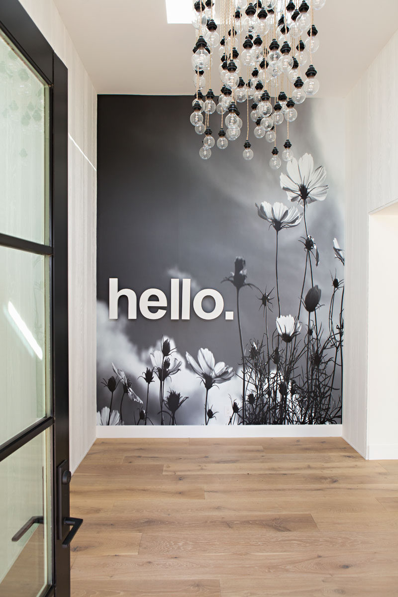 In this modern home entryway, you are greeted by an artistic bare-bulb light installation and a simple 'hello' mural covers the wall. #Entryway #Mural #Lighting