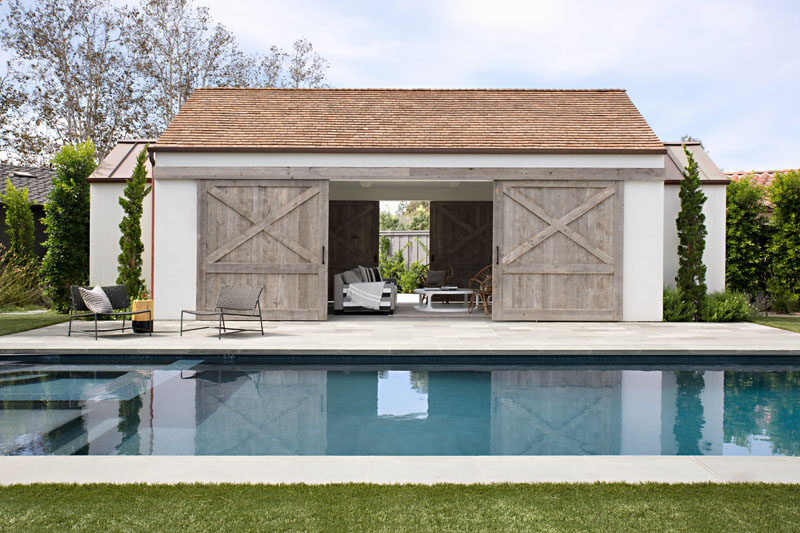 In this backyard, there a swimming pool with a pool house that has large, sliding wood barn doors that open to reveal another lounge area. #PoolHouse #SwimmingPool