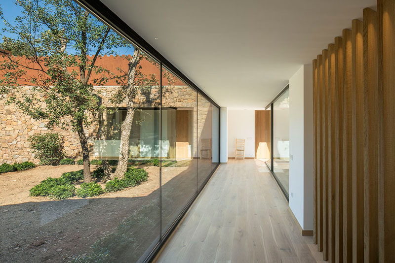 A wall of floor-to-ceiling windows with a view of a courtyard line this hallway that leads to the various areas of the home. #Hallway #Windows