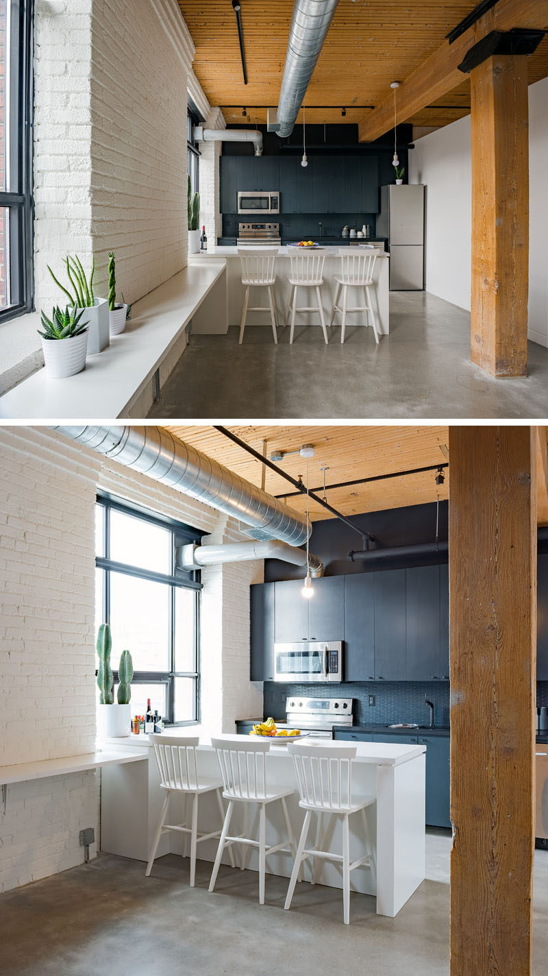 In this kitchen in a modern loft, there's a dark accent wall that draws your eye, while along the windows, a 'work bench' was added to create a space to work, display art or use when hosting a party. #KitchenDesign #Loft #InteriorDesign