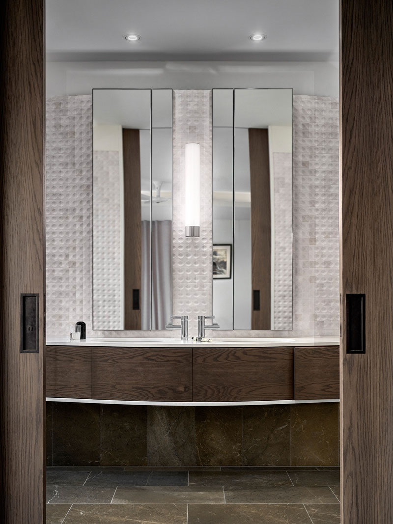 In this modern bathroom, a custom wood vanity is a strong contrast to the white marble tiles, while the mirrors make the space appear larger. #Bathroom #MarbleTiles #WoodVanity