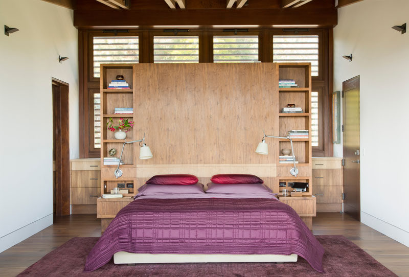 In this modern bedroom, a wood headboard has built-in bedside tables and open shelving for displaying personal items. #BedroomDesign #ModernBedroom #WoodHeadboard